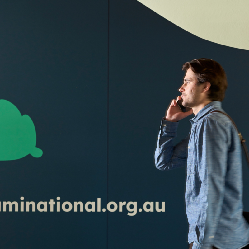 Person on mobile phone walking past a wall featuring the Neami logo and the website address ‘neaminational.org.au’