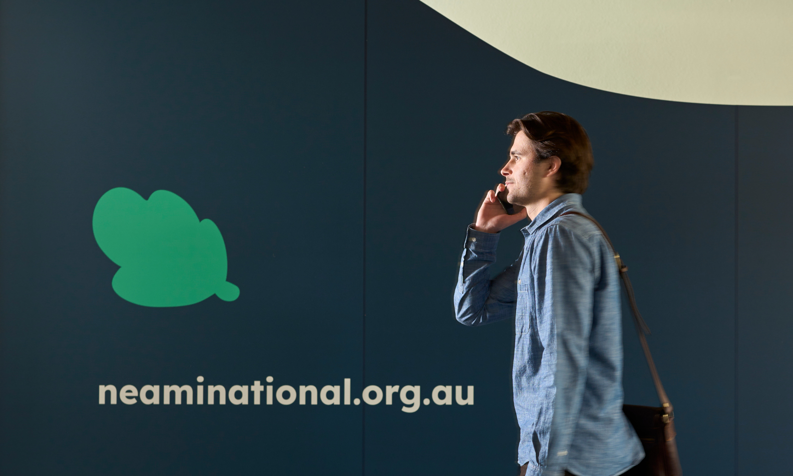 Person on mobile phone carrying bag walking past Neami National sign