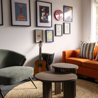 Comfortable couches and armchairs are around two small coffee tables, with a guitar and djembe by the wall. Framed posters, artworks and a dream catcher decorate the wall.