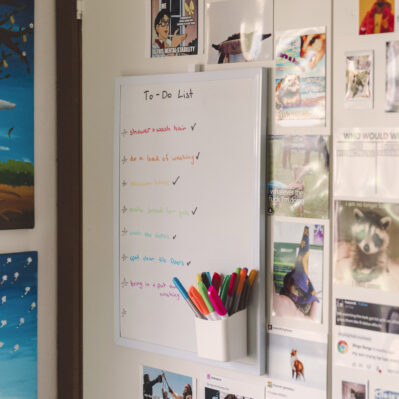 A whiteboard showing a resident’s to-do list. On the wall surrounding it a printed-out memes.