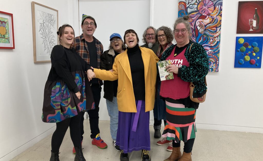 The Raiders of the Lost Art group smile in front of artworks at their exhibition launch.