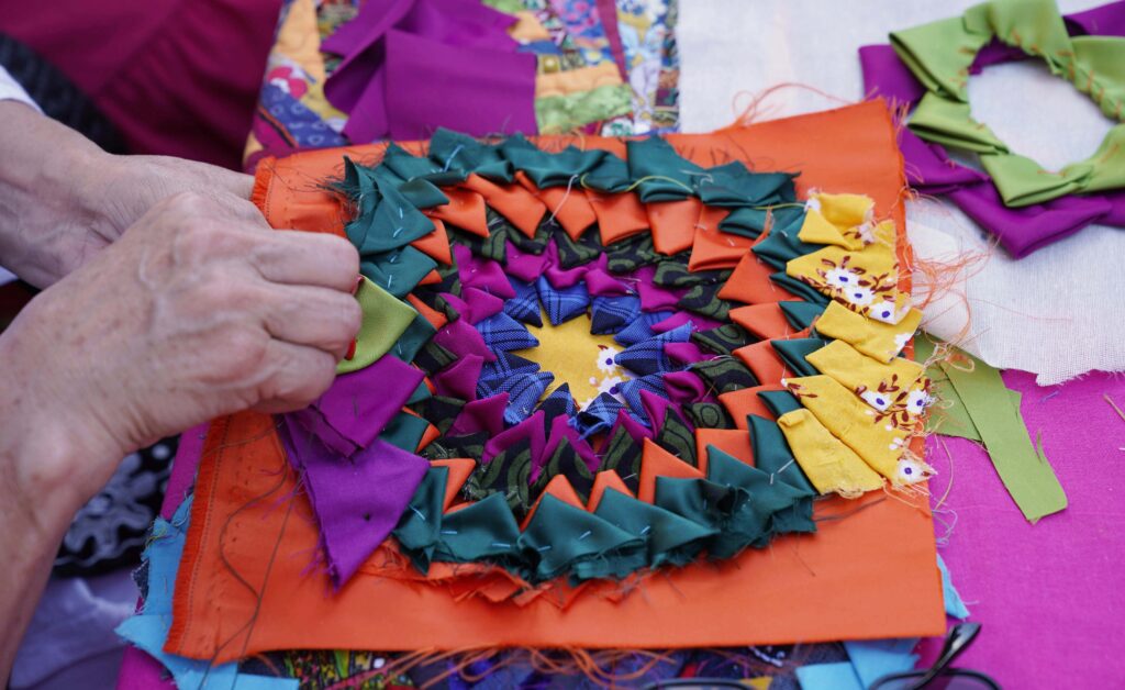 Close up of hands sewing a brightly-coloured pattern.