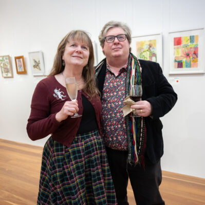 Two people looking at artwork on wall in gallery. Artists work in background: Sarah Donnell and Jenny Zitzke.