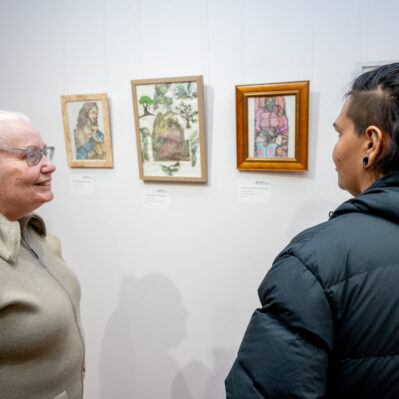 Artist and a person discussing artwork on gallery wall.
