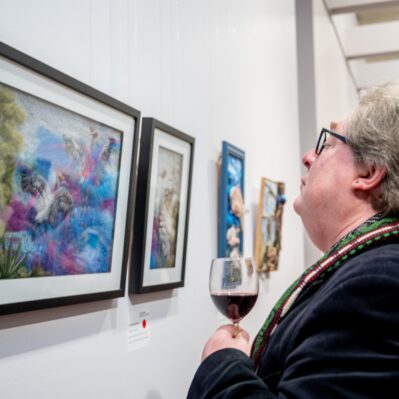 Person looking at artwork with glass of wine.