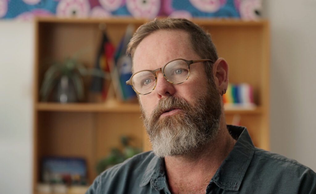 Man in office space looking off camera with a bookshelf in the background
