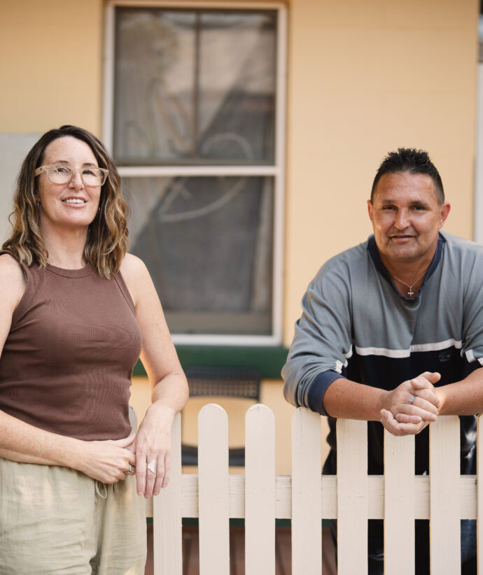 Two people standing outdoors against a picket fence