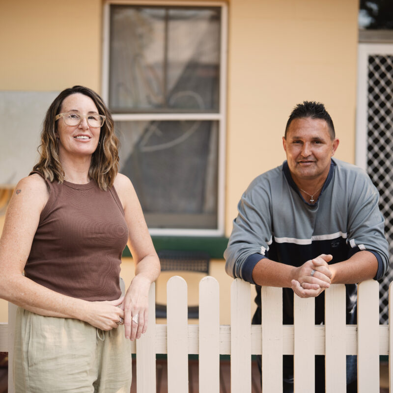 Two people standing outdoors against a picket fence
